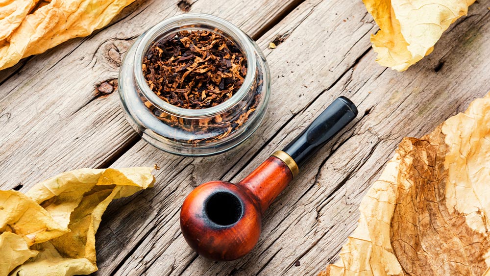 Tutunurile aromate de pipa intr-un bol de sticla langa o pipa din lemn